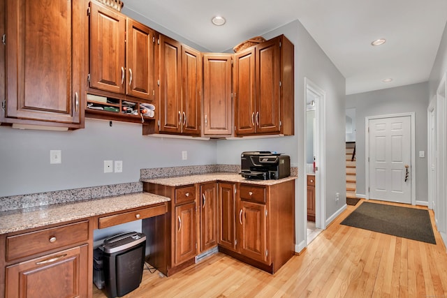 kitchen with baseboards, light stone countertops, light wood-type flooring, brown cabinets, and built in study area