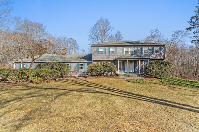 view of front of property with covered porch, a chimney, and a front yard