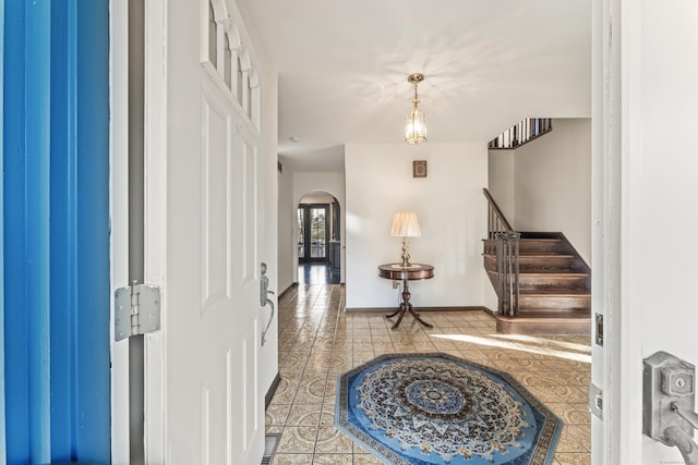 tiled foyer entrance with baseboards, arched walkways, and stairs