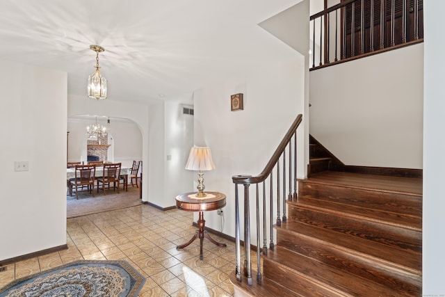 stairway with arched walkways, visible vents, baseboards, and an inviting chandelier