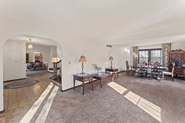 carpeted living room with baseboards, visible vents, arched walkways, and a chandelier