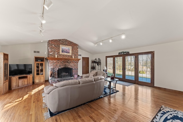 living room featuring visible vents, light wood finished floors, lofted ceiling, a fireplace, and french doors