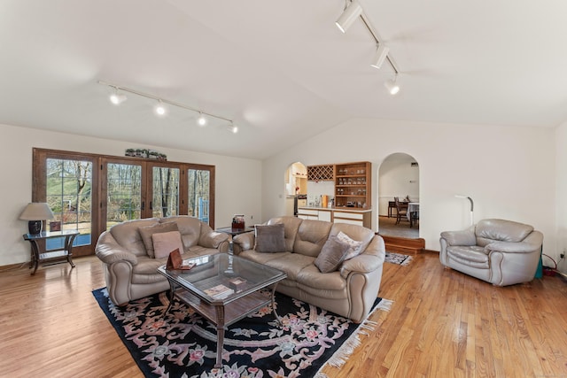 living area with arched walkways, french doors, light wood-style floors, and lofted ceiling