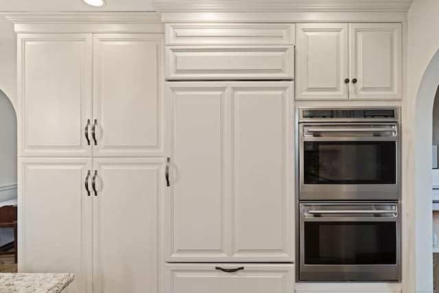 kitchen with arched walkways, double oven, white cabinets, and light stone countertops