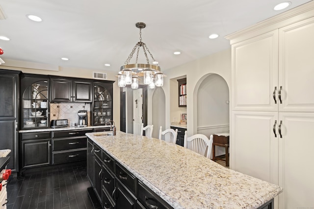 kitchen with visible vents, dark cabinets, arched walkways, a sink, and tasteful backsplash