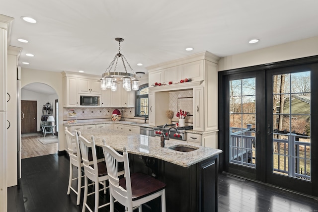 kitchen with black microwave, decorative backsplash, french doors, arched walkways, and a sink