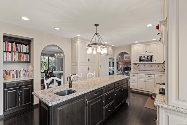 kitchen with built in microwave, white cabinets, arched walkways, and a sink