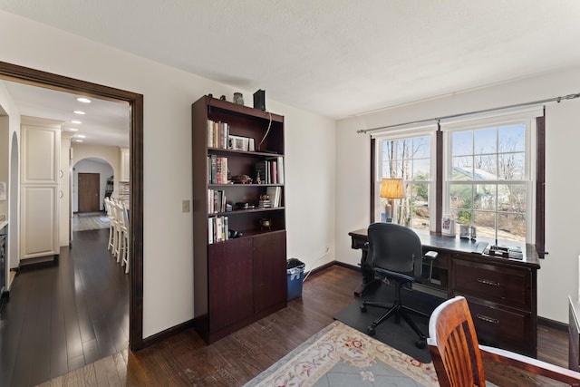 office space featuring baseboards, arched walkways, a textured ceiling, and dark wood finished floors