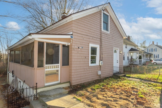 view of side of property featuring entry steps, a chimney, a sunroom, and fence