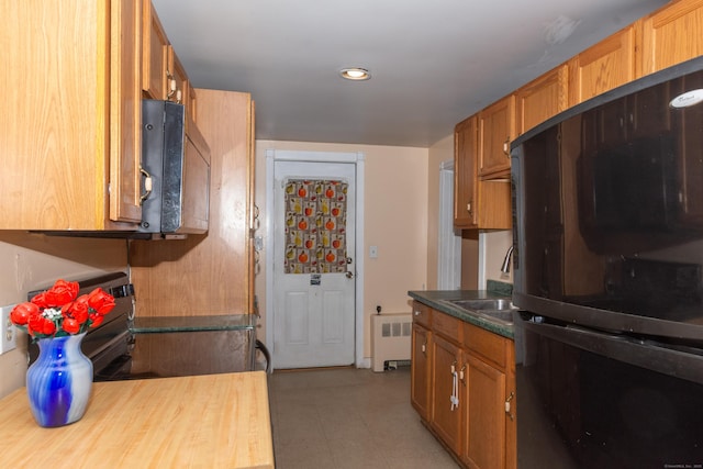 kitchen featuring brown cabinetry, radiator heating unit, freestanding refrigerator, a sink, and stainless steel microwave