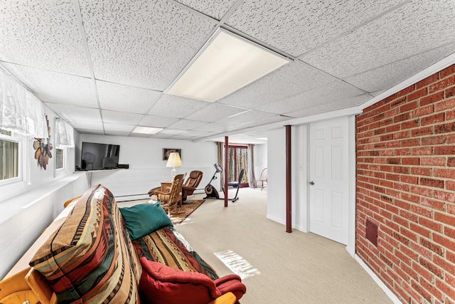 living area featuring a paneled ceiling, carpet, and brick wall