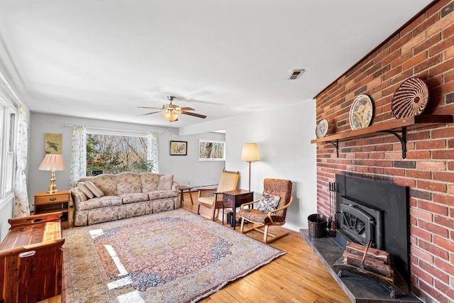 living area featuring visible vents, a wood stove, a ceiling fan, and wood finished floors