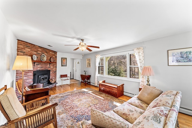 living room featuring wood finished floors, visible vents, a ceiling fan, a wood stove, and a baseboard heating unit