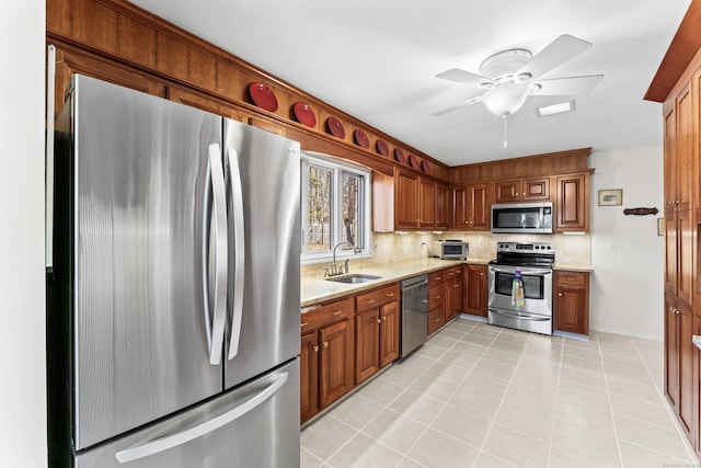 kitchen featuring light stone countertops, decorative backsplash, brown cabinets, stainless steel appliances, and a sink