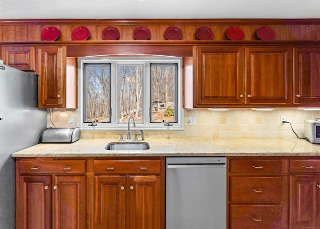 kitchen with light stone counters, brown cabinetry, a sink, decorative backsplash, and appliances with stainless steel finishes