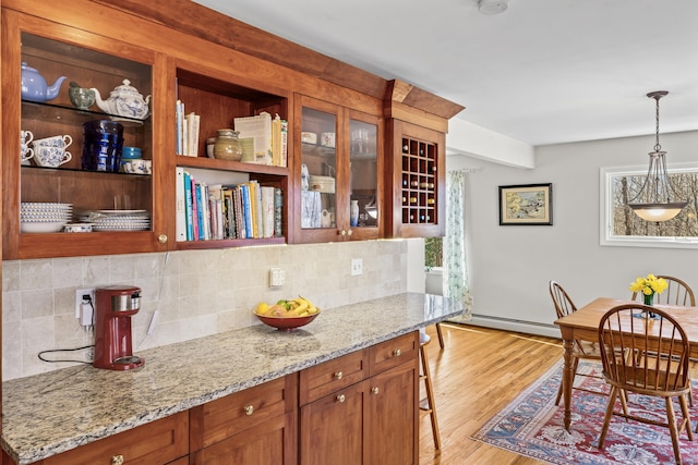 kitchen with tasteful backsplash, decorative light fixtures, light wood-type flooring, light stone counters, and a baseboard radiator