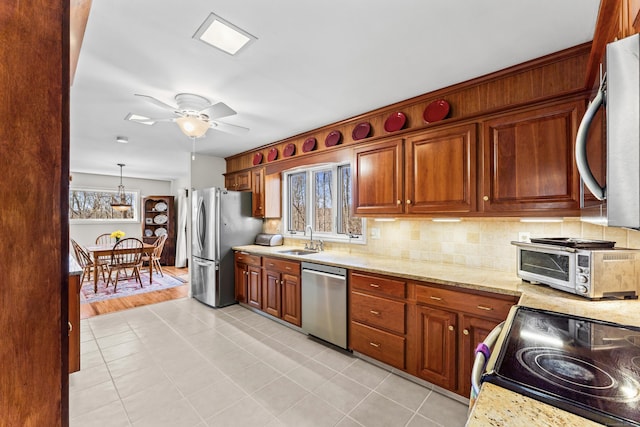 kitchen with backsplash, ceiling fan, light stone counters, appliances with stainless steel finishes, and a sink