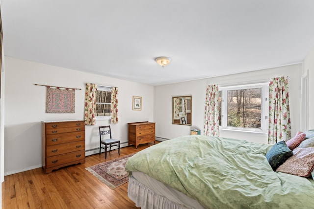 bedroom with a baseboard heating unit, light wood-type flooring, and baseboards