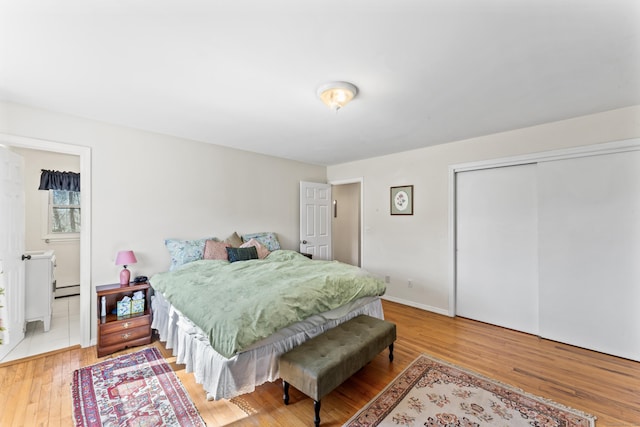 bedroom featuring hardwood / wood-style floors, baseboards, a closet, and a baseboard radiator