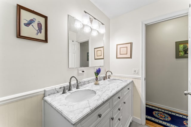 bathroom featuring double vanity, a wainscoted wall, and a sink