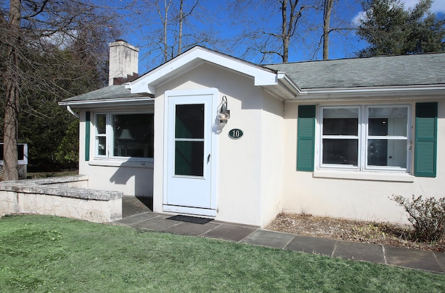 doorway to property with stucco siding, roof with shingles, and a chimney