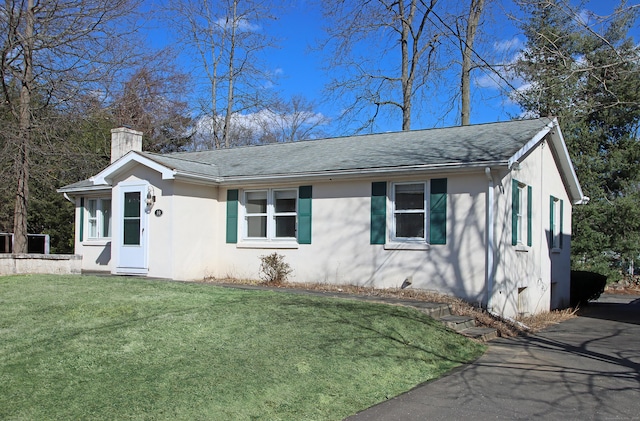 view of front of property featuring stucco siding, a front lawn, roof with shingles, and a chimney