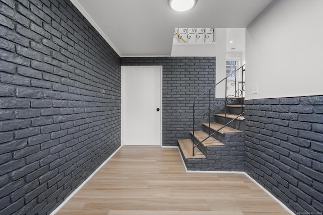 foyer entrance featuring stairway, brick wall, crown molding, and wood finished floors