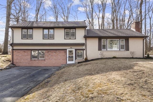 split level home with a shingled roof, aphalt driveway, brick siding, and a chimney