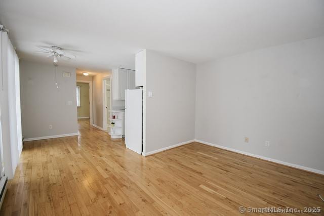 unfurnished living room with a baseboard heating unit, light wood-style flooring, and baseboards