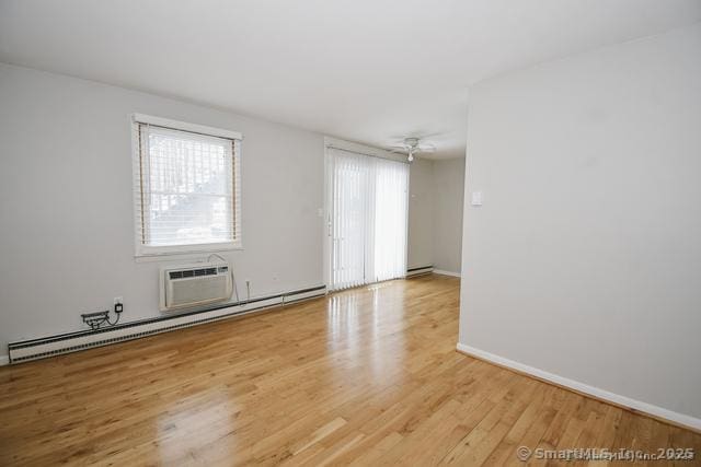 spare room with a baseboard radiator, baseboards, light wood-style floors, and an AC wall unit