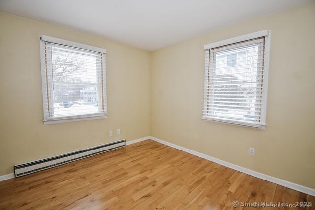 unfurnished room featuring a baseboard radiator, baseboards, and wood finished floors