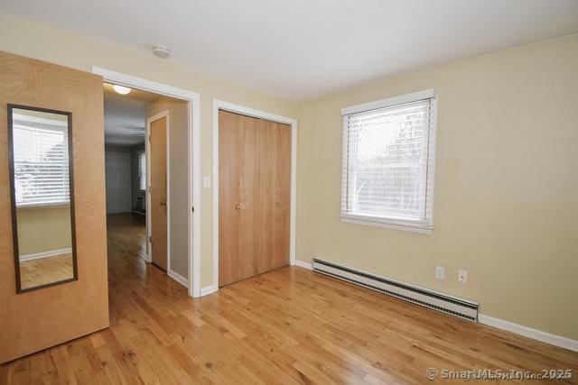 unfurnished bedroom with light wood finished floors, baseboards, a closet, and baseboard heating