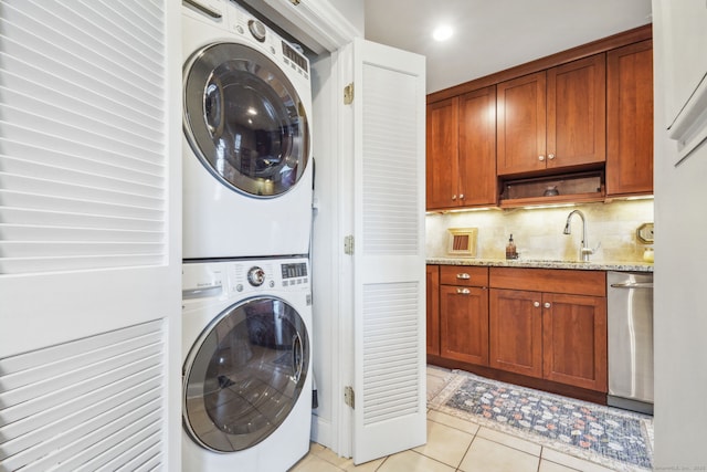 laundry area with laundry area, a sink, stacked washing maching and dryer, and light tile patterned floors