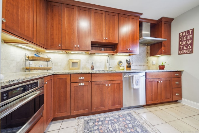 kitchen with light stone counters, light tile patterned flooring, a sink, appliances with stainless steel finishes, and wall chimney exhaust hood