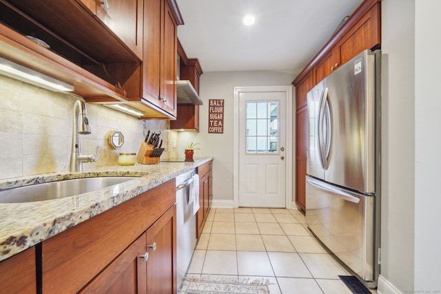 kitchen featuring light tile patterned floors, stainless steel appliances, decorative backsplash, a sink, and light stone countertops