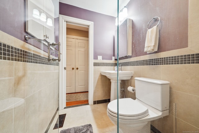 bathroom with toilet, a wainscoted wall, visible vents, tile walls, and tile patterned floors