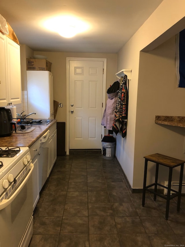 kitchen with white appliances, dark tile patterned flooring, a sink, white cabinets, and tasteful backsplash