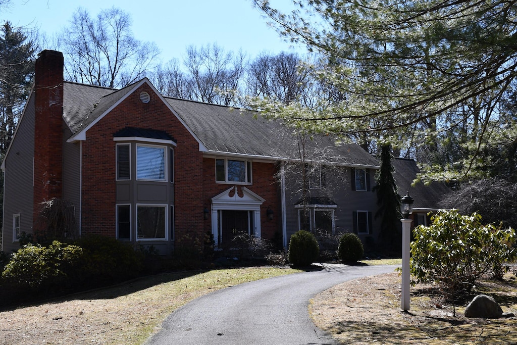 view of front facade with aphalt driveway, brick siding, roof with shingles, and a chimney