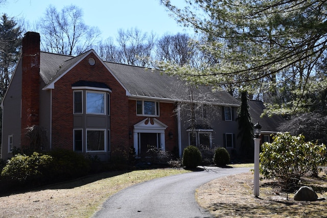 view of front facade with aphalt driveway, brick siding, roof with shingles, and a chimney