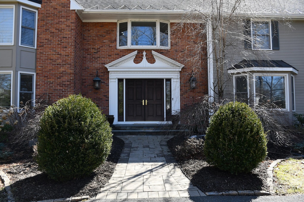 view of exterior entry featuring brick siding and roof with shingles