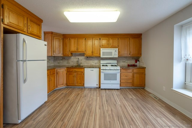 kitchen with white appliances, tasteful backsplash, visible vents, brown cabinetry, and a sink