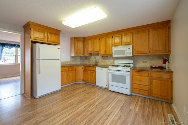 kitchen featuring light wood-style flooring, white appliances, a sink, brown cabinets, and tasteful backsplash