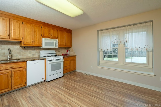 kitchen with light wood-style flooring, white appliances, a sink, visible vents, and decorative backsplash