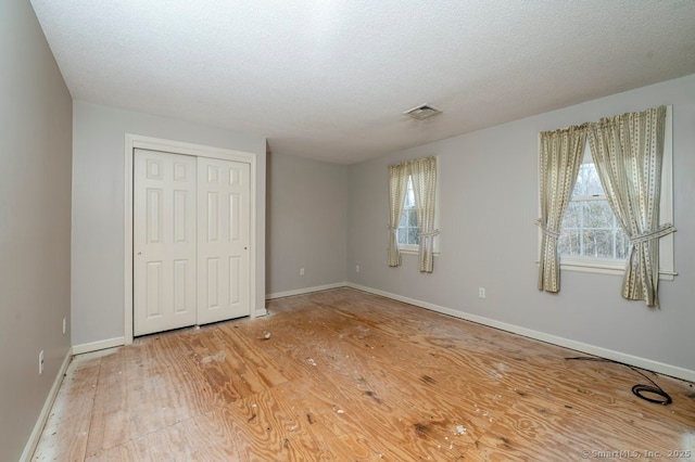 unfurnished bedroom with a textured ceiling, visible vents, baseboards, a closet, and light wood finished floors