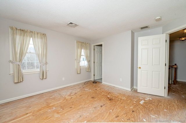 unfurnished room with a textured ceiling, wood finished floors, visible vents, and baseboards