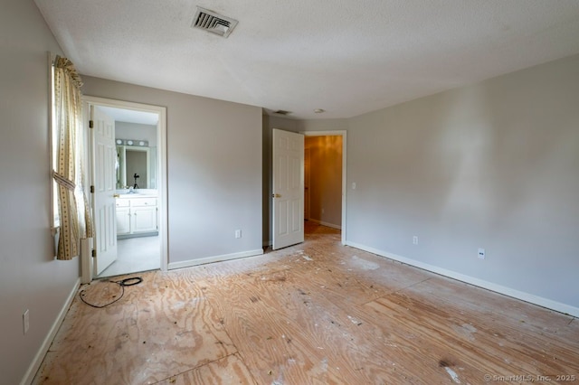 unfurnished bedroom with visible vents, a textured ceiling, baseboards, and ensuite bathroom