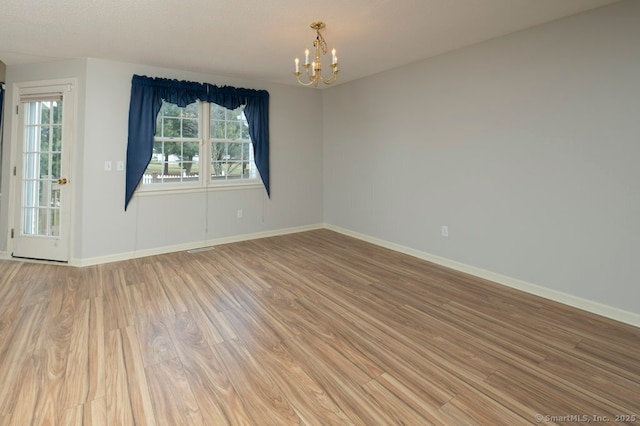 spare room featuring light wood-style floors, a notable chandelier, and baseboards