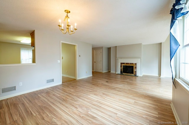 unfurnished living room featuring light wood finished floors, a fireplace with flush hearth, visible vents, and an inviting chandelier