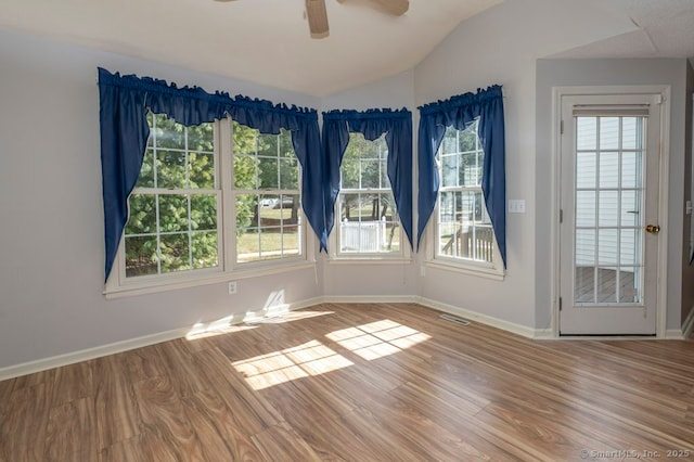 empty room with plenty of natural light, vaulted ceiling, and wood finished floors