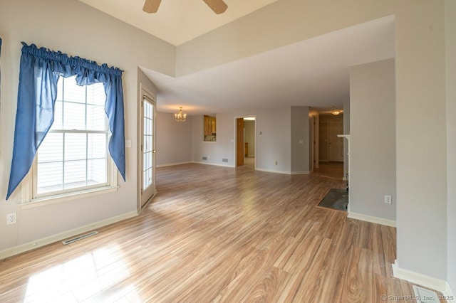 empty room featuring visible vents, light wood-style flooring, baseboards, and ceiling fan with notable chandelier